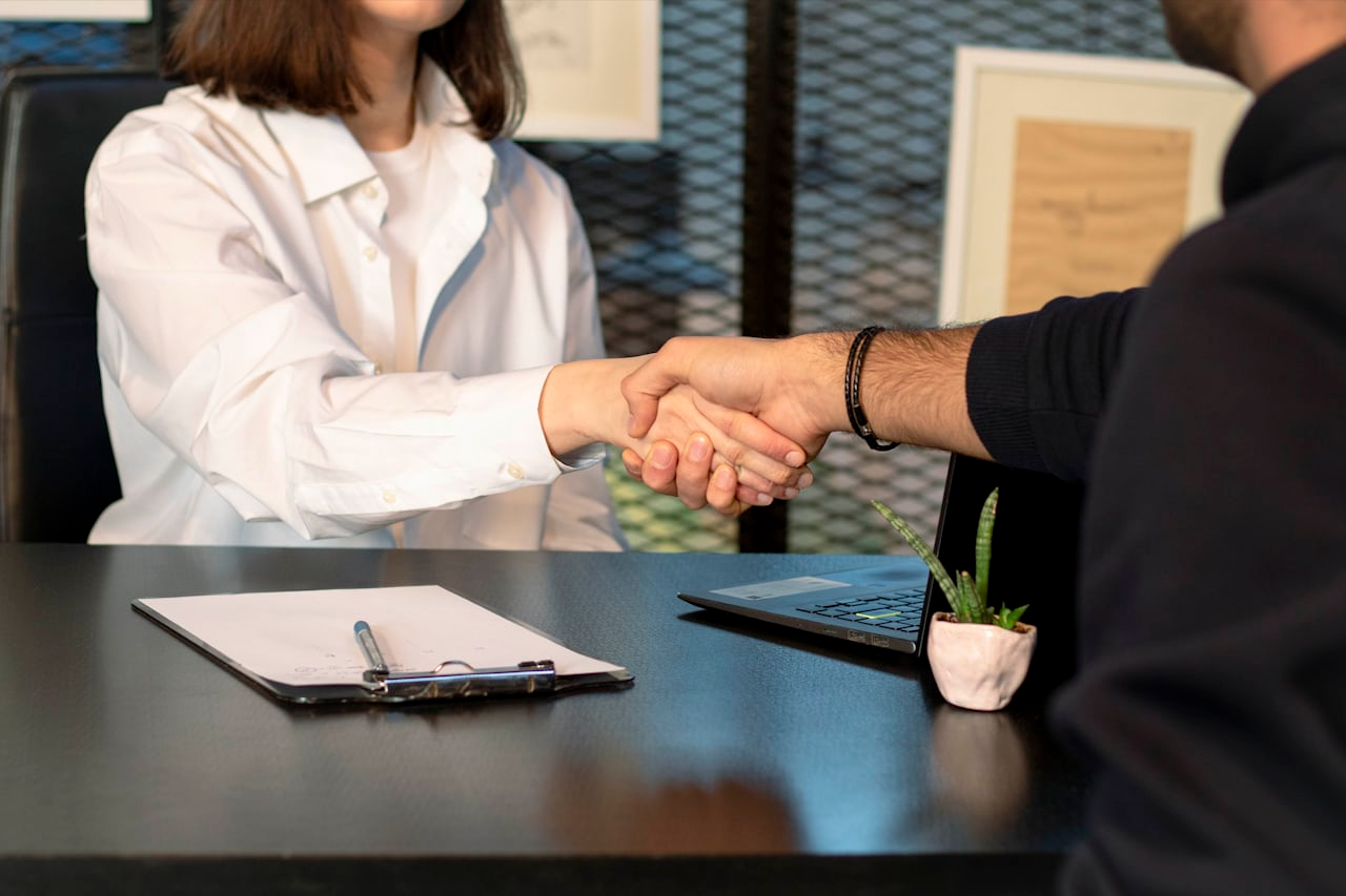 Two people shaking hands over a laptop after agreeing SaaS subscription terms