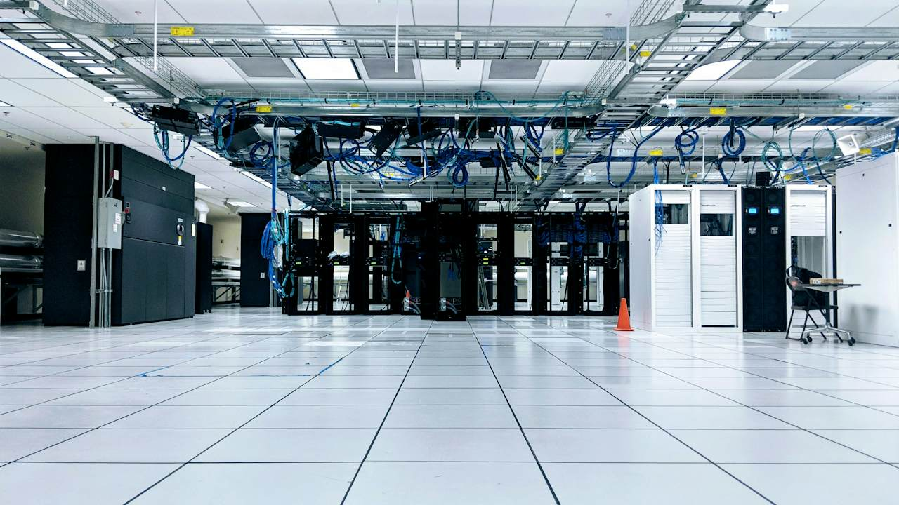 An empty data centre hall with rows of server cabinets and blue network cables overhead, representing the hosted service an SLA covers