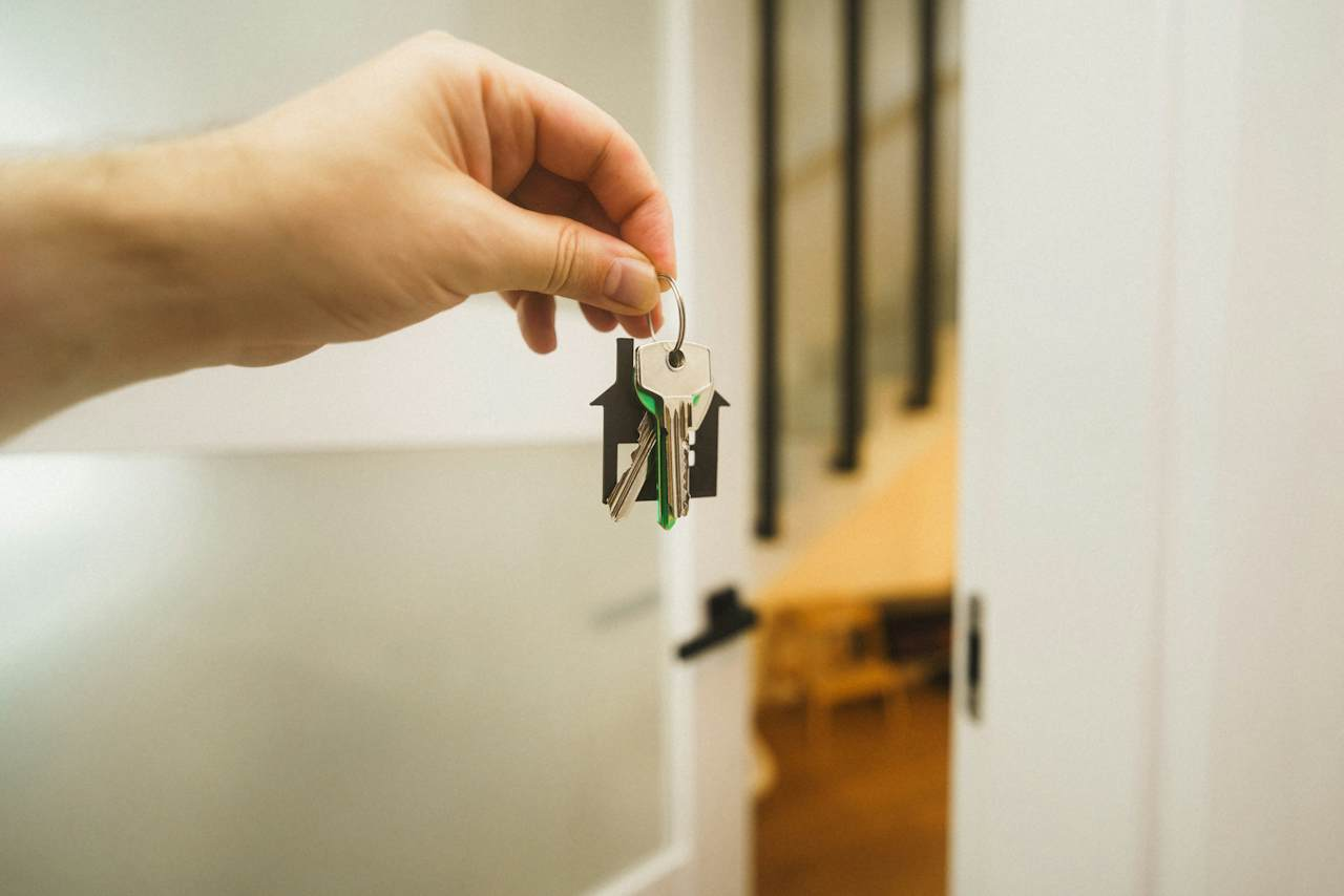 A hand holding a set of keys on a house-shaped fob in front of an open door, representing handing over access at the end of a contract